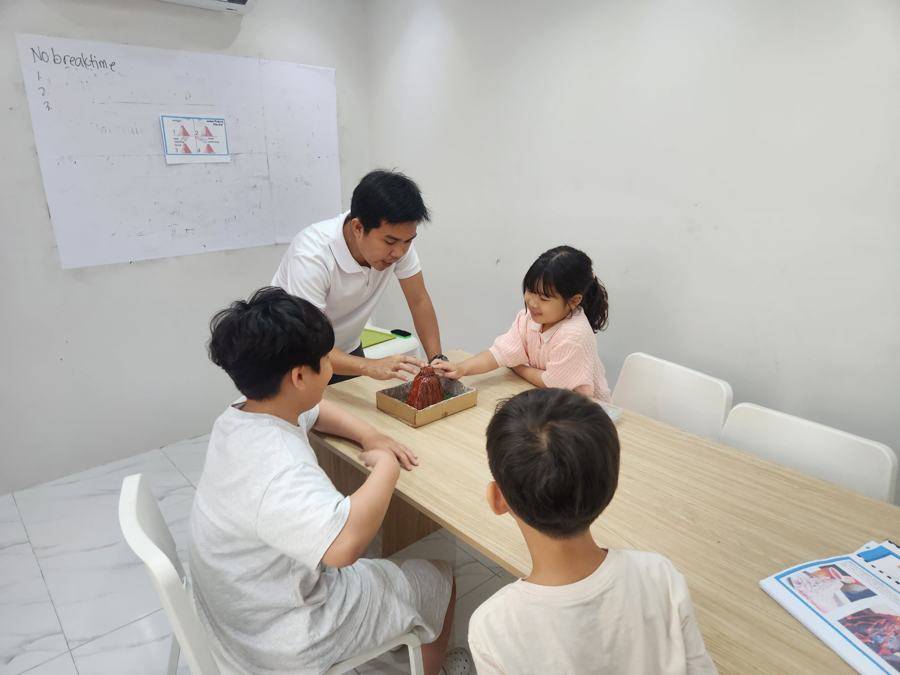 선생님과 학생 셋이 테이블에서 화산 모형을 함께 만드는 모습